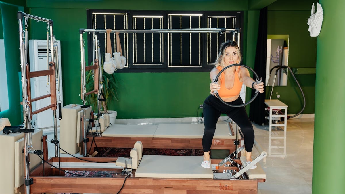 Fitness enthusiast practicing Pilates on a reformer machine in a modern, brightly lit studio.