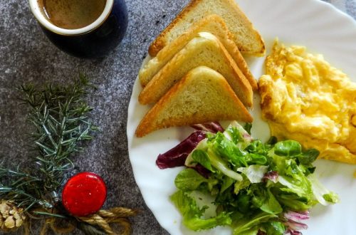 A breakfast plate with scrambled eggs, toast, salad, and coffee on a marble surface.