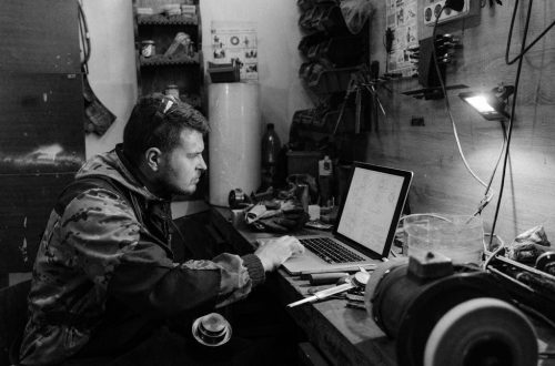 Black and white photo of a craftsman working on a laptop in a workshop setting.