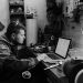 Black and white photo of a craftsman working on a laptop in a workshop setting.
